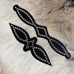 May include: Two black leather shapes with decorative stitching and silver studs. The shapes are in the form of a diamond and a teardrop.