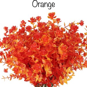 Könnte beinhalten: Ein Strauß orangefarbener Kunstblumen mit grünen Stielen. Die Blüten sind klein und haben ein zartes Aussehen. Der Text "Orange" steht über den Blumen.