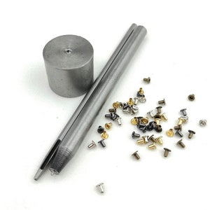 May include: A set of metal tools for setting eyelets, including a hammer, a punch, and a variety of eyelets in different colors.