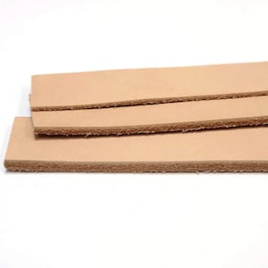 May include: Three pieces of light brown leather strips stacked on top of each other. The leather has a rough, unfinished edge.