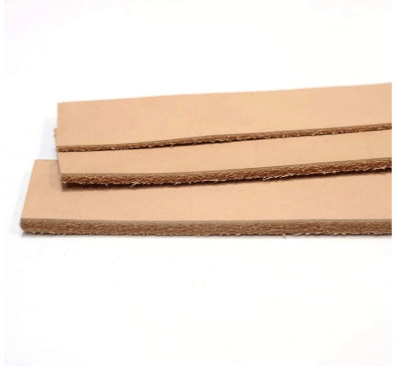 May include: Three pieces of light brown leather strips stacked on top of each other. The leather has a rough, unfinished edge.