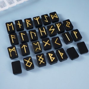 Puede incluir: Azulejos cuadrados negros con runas doradas, un conjunto de 24 runas, para la adivinación o la magia.