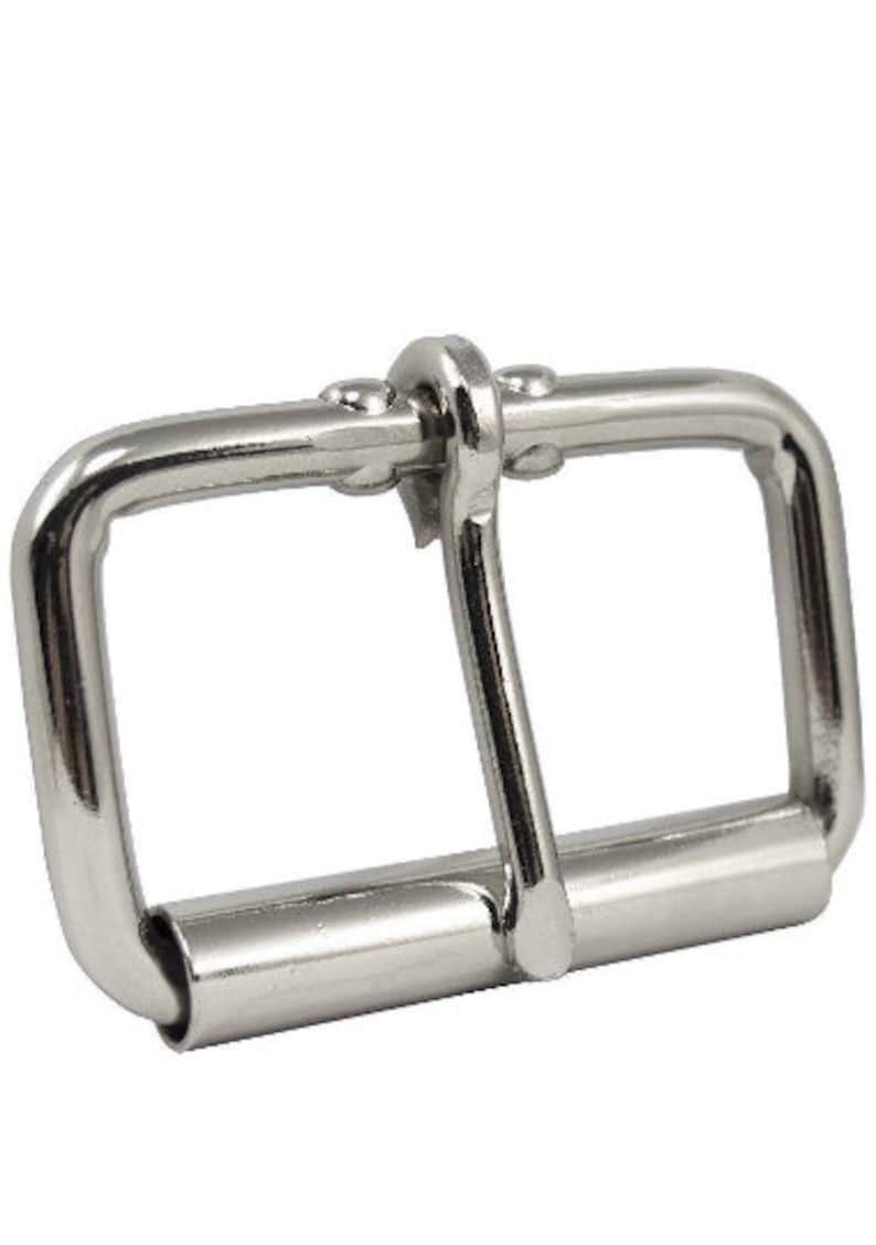May include: Silver metal buckle with a single prong. The buckle is designed for a belt or strap.
