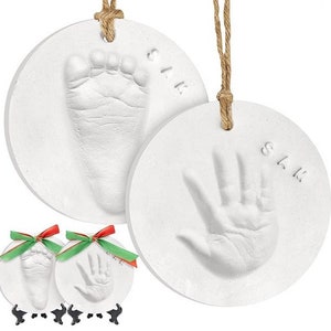 May include: Two white ceramic ornaments with a handprint and footprint, each with the name "Sam" written on them. The ornaments are attached to twine.