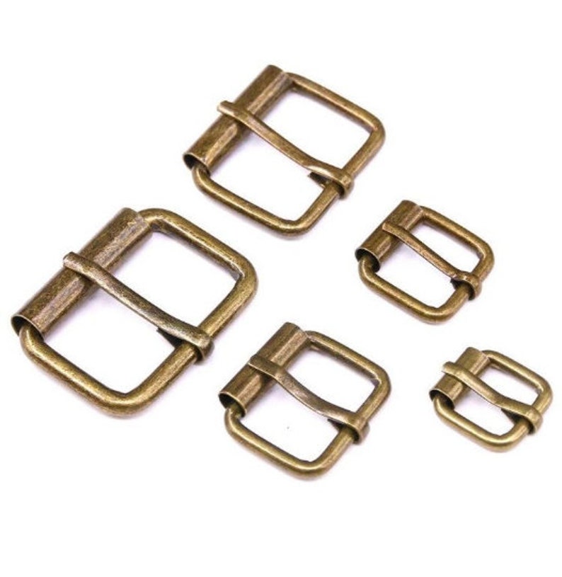 May include: Five antique gold-toned metal belt buckles of varying sizes. The buckles are all rectangular in shape with a center bar and two prongs.