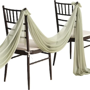 Puede incluir: Dos sillas de madera marrón oscuro con cojines beige claro están adornadas con tela verde salvia fluida. La tela está atada a los respaldos de las sillas con lazos y se extiende entre las sillas, creando un elegante efecto decorativo.