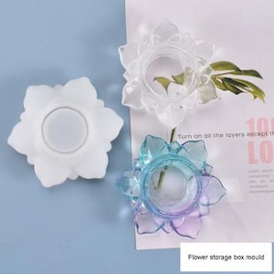 May include: Three flower-shaped silicone moulds for making resin crafts. The moulds are white, clear, and blue and purple. The text "Flower storage box mould" is visible at the bottom of the image.