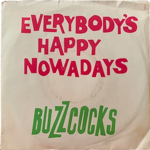 Peut inclure: Pochette de disque vintage avec le texte "EVERYBODY'S HAPPY NOWADAYS" en rouge et "BUZZCOCKS" en vert. Le fond est blanc cassé avec des traces d'usure. Le design est simple et les couleurs vives.