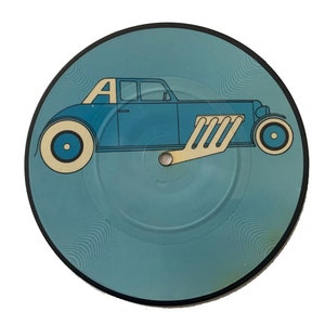 May include: A vinyl record with a light blue background and a stylized blue car graphic. The car has a beige exhaust pipe and the letter "A" on the roof. The record has a black border and a central hole.