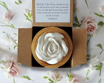 May include: A white ceramic rose diffuser sits on a wooden base. The diffuser is in a cardboard box with instructions on how to use it. "Enjoy the aroma of your favourite essential oils with this ceramic oil diffuser, which offers a subtle aroma, that lasts up to 8 hours, depending on the type of essential oil used. HOW TO USE: Put about 10 drops of essential oil or spray your favourite perfume onto the ceramic disc, which will absorb it and slowly release the aroma. Please note that essential oils might lead to discolouration of the diffuser over time. Do not wash petit-grain.co.uk"