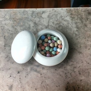 May include: A white ceramic container with a lid, filled with colourful round beads. The container has a speckled texture.