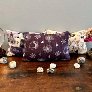 May include: Three decorative pillows with different patterns. The first pillow has a white background with a black and white tarot card design. The second pillow has a dark purple background with a white moon and star design. The third pillow has a white background with a black and white butterfly design.