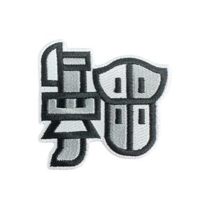 May include: Embroidered patch featuring a stylized Japanese character in shades of gray and black. The design has a shield-like shape on the right and a more angular form on the left, all outlined in black.