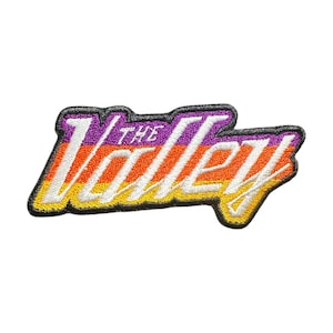 May include: Embroidered patch with the text "The Valley" in a retro style. The patch features a gradient of colors, including purple, orange, white, and yellow, with a black border. The patch is likely designed for clothing or accessories.