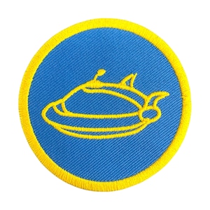 Pode incluir: Patch bordado circular com um design de nave espacial amarela sobre fundo azul, contornado por uma borda amarela. Perfeito para personalizar roupas ou acessórios.