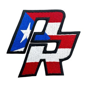 Puede incluir: Un parche bordado con las letras "PR" en una fuente en negrita y de bloque. Las letras están delineadas en negro y el fondo es la bandera de Puerto Rico, con colores rojo, blanco y azul.