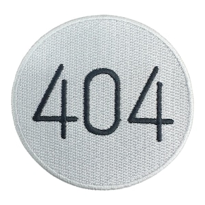 May include: A circular, embroidered patch with a light gray background. The number "404" is stitched in black, centered on the patch. The patch has a textured appearance, suggesting a fabric material. The design is simple and modern.