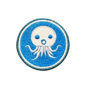 May include: A round, embroidered patch featuring a cartoon octopus design. The octopus is white with blue eyes and tentacles, set against a blue background with a white border. The patch is likely for clothing or accessories.
