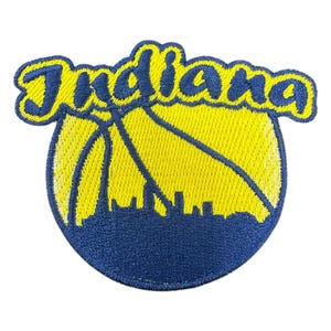 Op de afbeelding: Geborduurde patch met het woord "Indiana" in gele letters boven een geel basketbalontwerp. De basketbal heeft blauwe accenten en een blauw silhouet van de skyline aan de onderkant. Geschikt voor kleding.