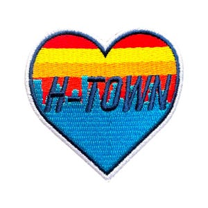 May include: A heart-shaped patch with a blue, yellow, orange, and red sunset design. The text "H-TOWN" is embroidered in navy blue.