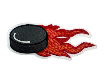 May include: Embroidered patch showing a black hockey puck with a white stripe, followed by a stylized red and orange flame design. The patch has a white border, suitable for application on clothing or accessories.