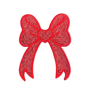 Puede incluir: Un lazo rojo con purpurina con un corazón en el centro. El lazo es una decoración festiva para regalos, manualidades y otros proyectos.