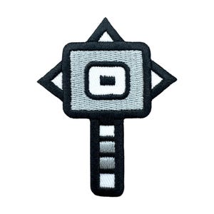 Puede incluir: Parche bordado con un diseño geométrico en tonos grises, negros y blancos. El parche tiene un centro cuadrado con una forma rectangular en el interior, flanqueado por cuatro formas de flecha. Un tallo vertical con barras de gradiente gris completa el diseño.