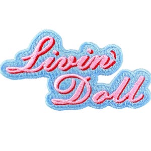 May include: A blue and pink embroidered patch with the text "Livin' Doll" in a cursive font.