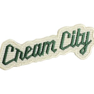 May include: White embroidered patch with the text "Cream City" in green lettering.