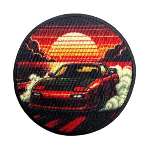 May include: Round patch featuring a red sports car drifting, with smoke billowing from the tires. The background depicts a sunset with a yellow sun and red and black clouds. The patch has a black border.