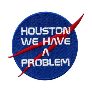 May include: A blue and red embroidered patch with the text "Houston We Have A Problem" in white lettering. The patch features a red crescent shape against a blue circle.