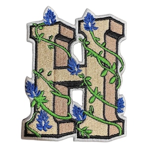 May include: An embroidered iron-on patch featuring the letter H in a beige color with a vine and blue flower design.