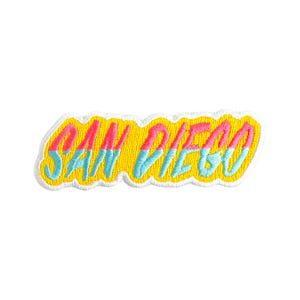 May include: Embroidered patch with the text "SAN DIEGO" in pink and blue, outlined in white, on a yellow background. The patch has a wavy border, suitable for clothing or accessories.