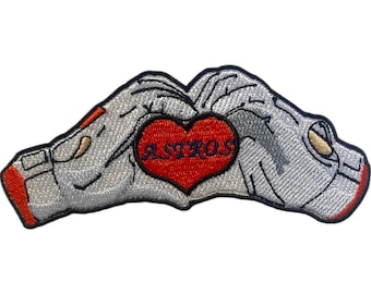 May include: Embroidered patch with two hands forming a heart shape, with the word "ASTROS" inside the heart. The hands are gray, the heart is red, and the text is blue.