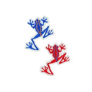 Può includere: Due toppe ricamate a forma di rana. Una rana è blu con una striscia arancione sulla schiena, l'altra è rossa con una striscia rossa. Entrambe hanno contorni bianchi su sfondo bianco.