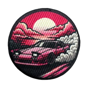 May include: Embroidered patch depicting a pink sports car drifting, set against a sunset. The design includes a white sun, pink clouds, and white smoke. The patch has a black border.