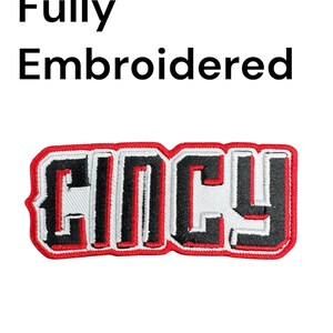 May include: Fully embroidered patch with the word "Cincy" in black, white, and red. The patch measures 3 inches wide and has an iron-on backing. The text "Fully Embroidered" is above the patch.