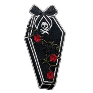 May include: Black embroidered iron-on patch of a coffin with a skull and crossbones inside, surrounded by red roses and vines.