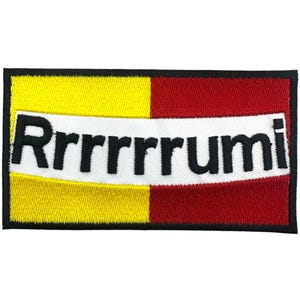 Puede incluir: Parche bordado con la palabra "Rrrrrrumi" en negro sobre una pancarta blanca. El parche tiene un fondo amarillo y rojo, con un borde negro.