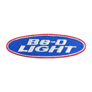 Könnte beinhalten: Ovaler, gestickter Aufnäher mit dem weißen Schriftzug "Be-D LIGHT" auf blauem Grund. Der Aufnäher hat einen roten und weißen Rand.