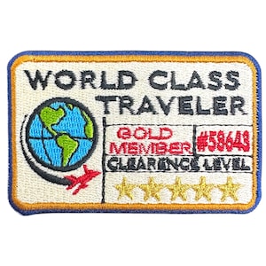 May include: A blue and yellow embroidered patch with the text "World Class Traveler" and a globe graphic. The patch also includes the text "Gold Member #58643 Clearance Level" and five gold stars.