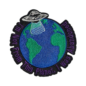 May include: Embroidered patch with a black background, a green and blue globe, a grey UFO, and purple text that reads "I Was Abandoned From This Planet, I'm Not From This Planet".