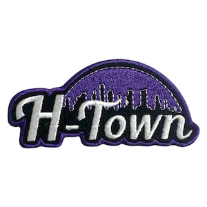 Könnte beinhalten: Lila und weiß gestickter Patch mit dem Text "H-Town" und einem Stadtbild-Design.