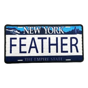 May include: A blue and white embroidered patch with the text "NEW YORK" and "FEATHER" in a white rectangle with a blue border. The text "THE EMPIRE STATE" is below the rectangle.