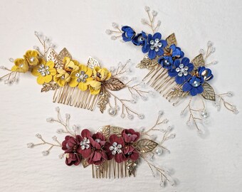 May include: Three floral hair combs in yellow, blue, and burgundy. Each comb features fabric flowers, gold-toned leaves, and crystal accents. The combs are designed with a classic comb base for easy styling.