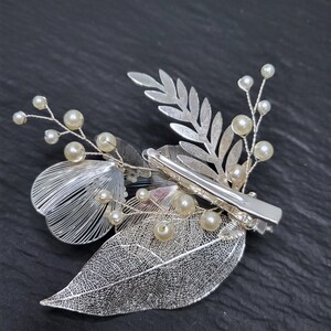 May include: Silver hair clip with a floral design and pearl accents. The clip features a delicate fern leaf, a flower with a pearl center, and a row of pearls along the stem.