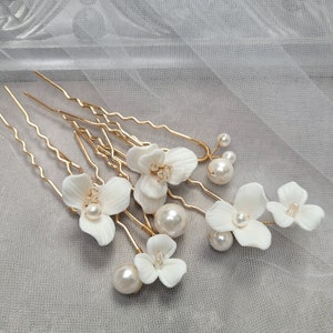 May include: Set of six gold hair pins with white ceramic flowers and pearl accents. The flowers have a delicate, slightly ruffled appearance.