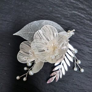 May include: A delicate white floral hair comb with pearl accents and a leaf design. The comb is made of wire and beads, and it has a vintage aesthetic.