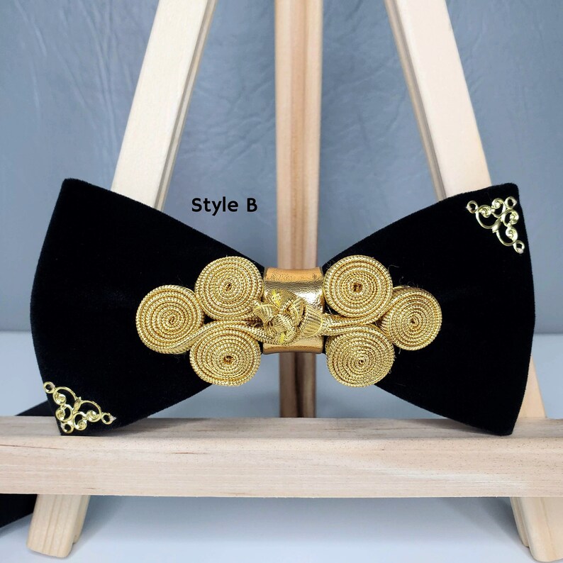 May include: Black velvet bow tie with a gold decorative design. The design features a series of interlocking circles and a gold buckle. The bow tie is labelled "Style B".