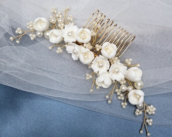 May include: A white floral hair comb with pearl accents. The comb is made of gold wire and has a cluster of white flowers with pearl centers. The comb is perfect for adding a touch of elegance to any hairstyle.